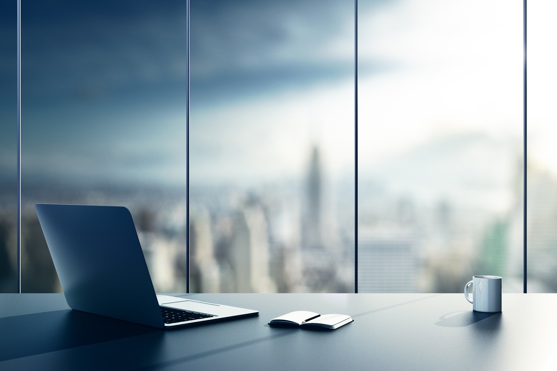 a laptop sits on a desk in front of a window with a cityscape in the background